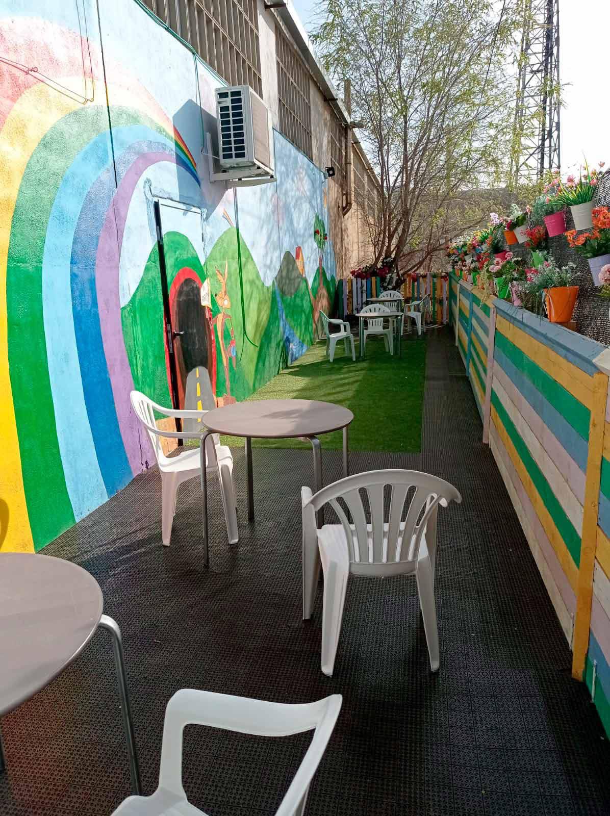 Terraza exterior con mural de arcoíris, mesas y sillas