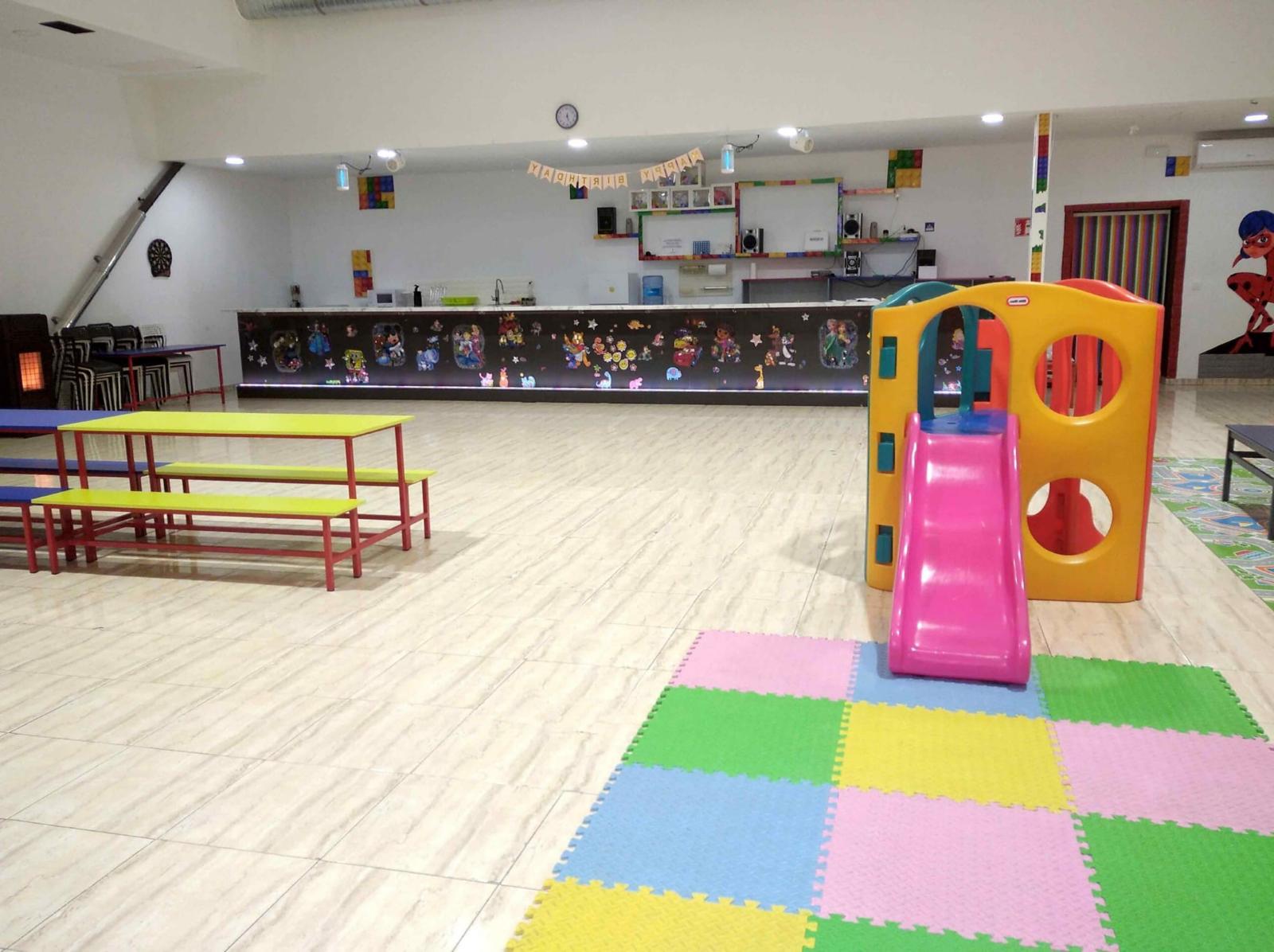 Salón con barra decorada, tobogán rosa y suelo de goma eva