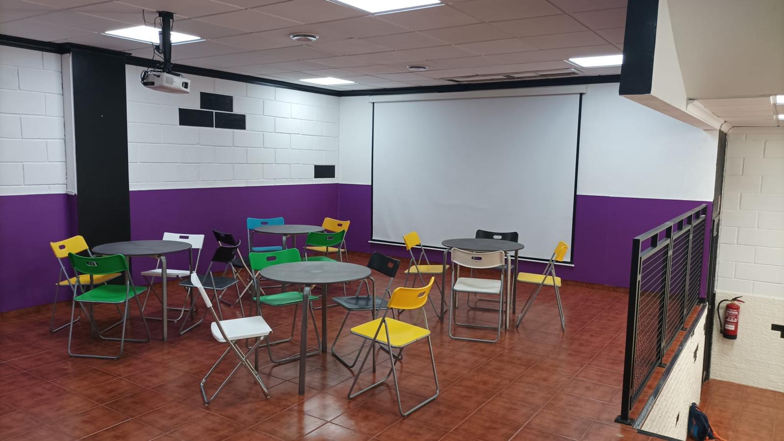 Sala polivalente con pantalla de proyección y sillas de colores para eventos